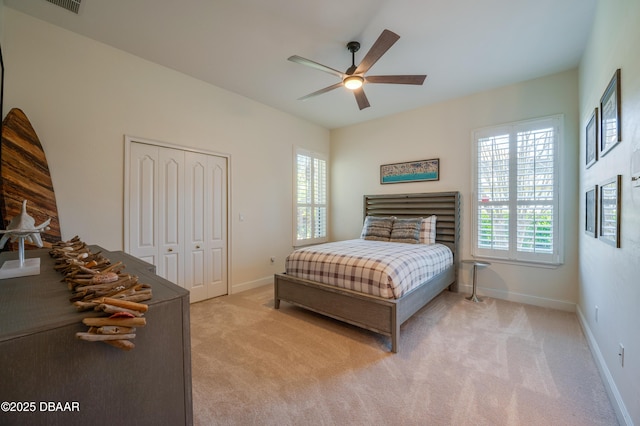 bedroom with a closet, baseboards, light colored carpet, and ceiling fan