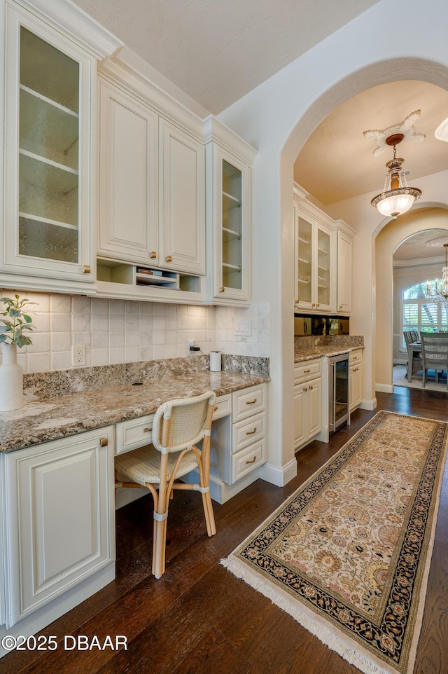 kitchen with light stone countertops, dark wood finished floors, arched walkways, wine cooler, and tasteful backsplash