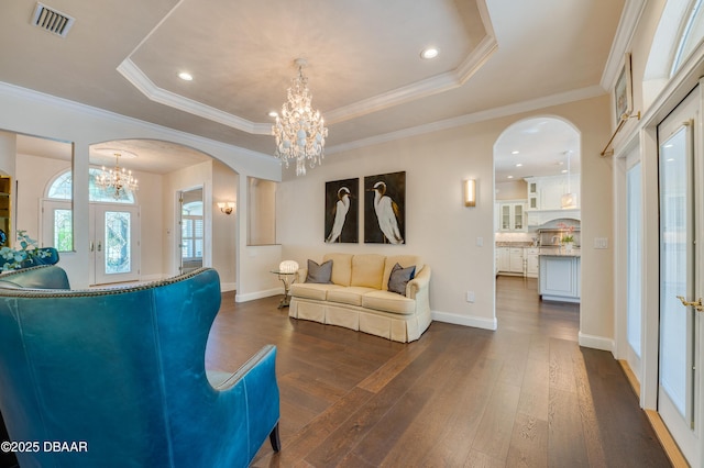 living area with visible vents, a raised ceiling, arched walkways, and an inviting chandelier