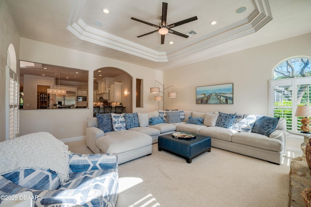 living area with crown molding, carpet, ceiling fan, arched walkways, and a raised ceiling