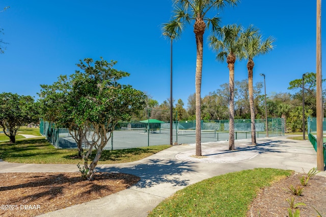 view of property's community featuring a tennis court and fence