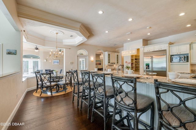 kitchen with light stone countertops, dark wood finished floors, built in appliances, crown molding, and a kitchen breakfast bar