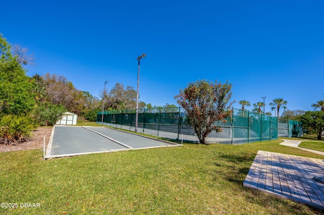 view of tennis court with an outbuilding, a yard, and fence