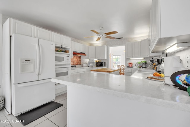 kitchen with light tile patterned flooring, sink, kitchen peninsula, white appliances, and white cabinets