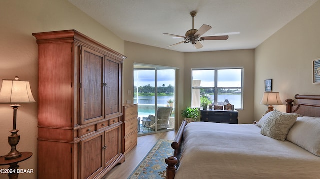 bedroom with access to exterior, ceiling fan, light hardwood / wood-style flooring, and a water view