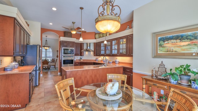 kitchen with stainless steel appliances, ceiling fan, sink, wall chimney range hood, and light tile patterned floors