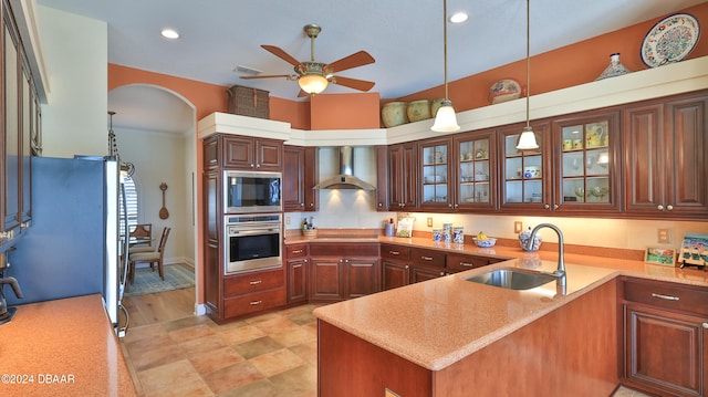 kitchen with ceiling fan, sink, wall chimney exhaust hood, stainless steel appliances, and kitchen peninsula