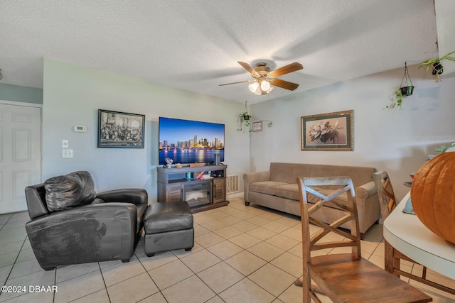 tiled living room featuring a textured ceiling, ceiling fan, and a fireplace