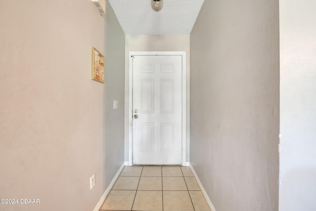 doorway with a textured ceiling and light tile patterned flooring