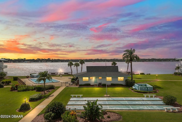 back house at dusk with a water view, a yard, and a fenced in pool