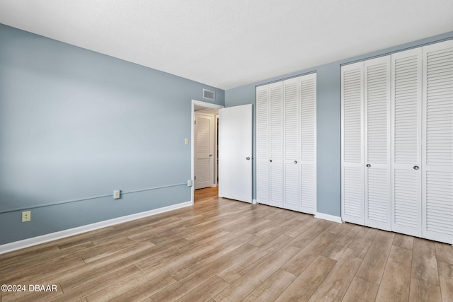 unfurnished bedroom featuring two closets, a textured ceiling, and light hardwood / wood-style flooring