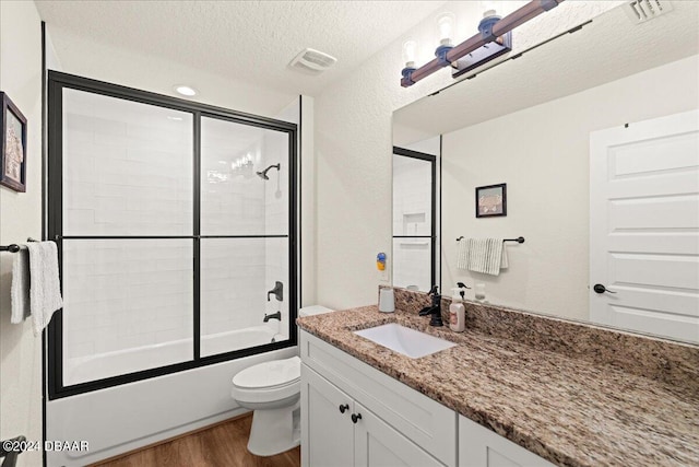 full bathroom featuring toilet, a textured ceiling, hardwood / wood-style flooring, shower / bath combination with glass door, and vanity