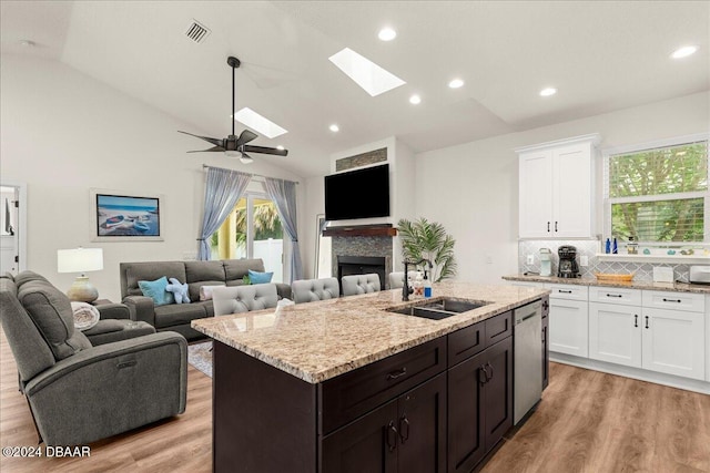 kitchen with a center island with sink, backsplash, vaulted ceiling with skylight, a fireplace, and light hardwood / wood-style flooring