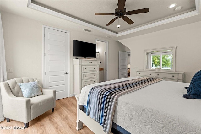 bedroom with light hardwood / wood-style floors, ornamental molding, a tray ceiling, and ceiling fan