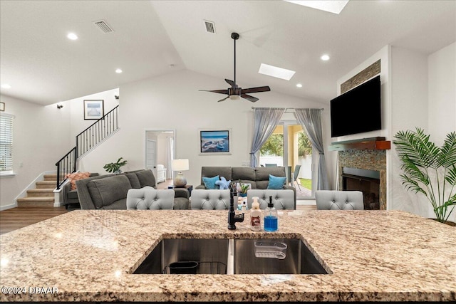 kitchen with light stone countertops, a tiled fireplace, hardwood / wood-style floors, lofted ceiling with skylight, and ceiling fan