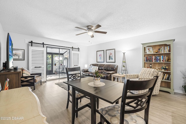 dining space featuring a barn door, ceiling fan, light hardwood / wood-style flooring, and a textured ceiling