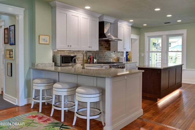 kitchen featuring dark wood-type flooring, white cabinets, wall chimney exhaust hood, appliances with stainless steel finishes, and kitchen peninsula