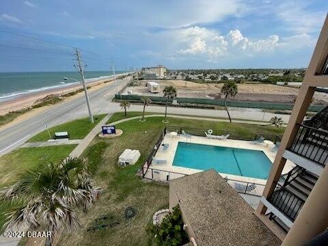 view of pool with a patio, a water view, a lawn, and a beach view