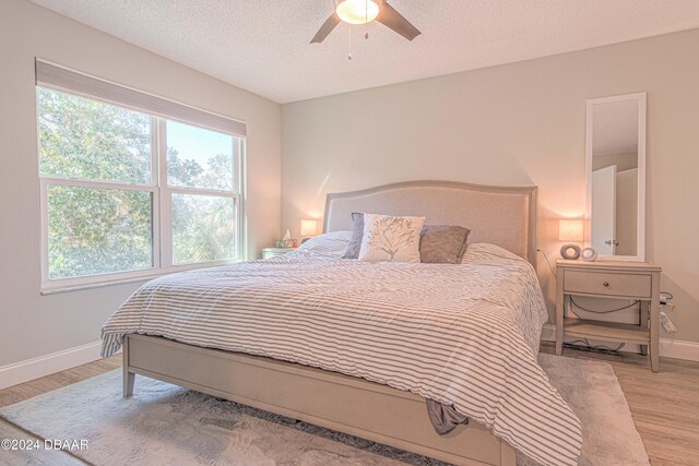 bedroom featuring light wood-type flooring, multiple windows, a textured ceiling, and ceiling fan