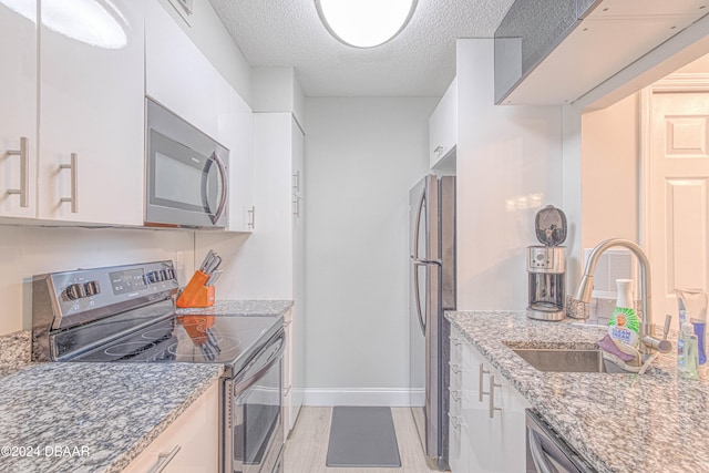 kitchen with stainless steel appliances, stone counters, white cabinetry, and sink