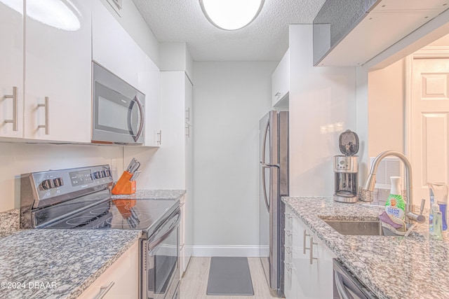 1401 S Palmetto Ave Unit 318, Daytona Beach, FL 32114 - kitchen with appliances with stainless steel finishes, a sink, a textured ceiling, white cabinetry, and light stone counters