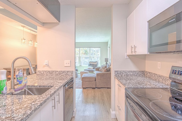 kitchen with white cabinets, stainless steel appliances, light hardwood / wood-style floors, and light stone counters