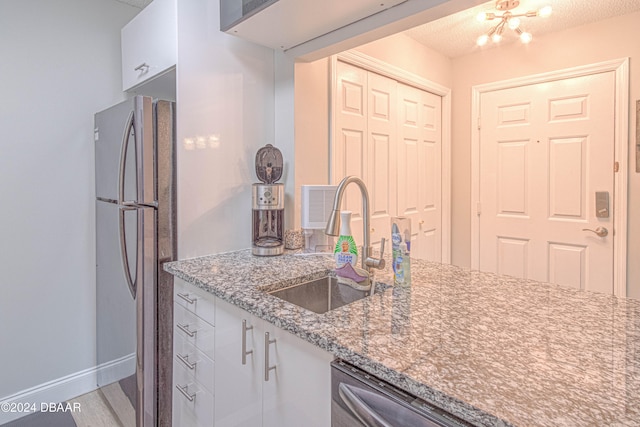 kitchen featuring stainless steel appliances, light stone counters, white cabinets, a textured ceiling, and sink