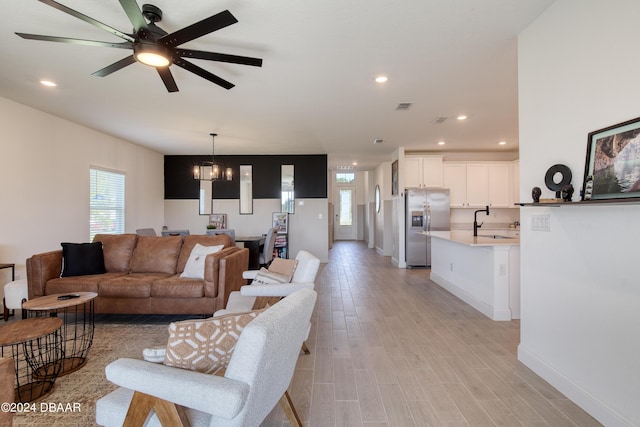 living area with ceiling fan with notable chandelier, light wood-type flooring, baseboards, and recessed lighting