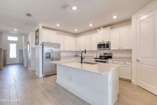 kitchen with visible vents, an island with sink, appliances with stainless steel finishes, light stone counters, and a sink