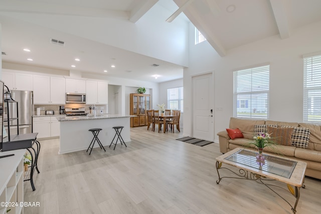 living room featuring high vaulted ceiling, light hardwood / wood-style floors, beamed ceiling, and a healthy amount of sunlight