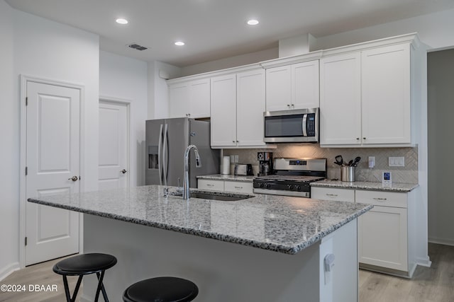 kitchen with stainless steel appliances, white cabinets, sink, and an island with sink