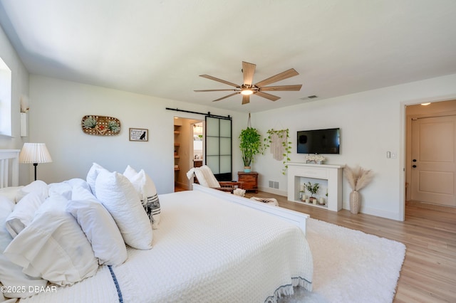 bedroom with visible vents, a ceiling fan, a barn door, light wood-style floors, and baseboards