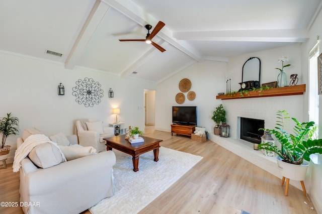 living room with visible vents, lofted ceiling with beams, light wood finished floors, a brick fireplace, and ceiling fan