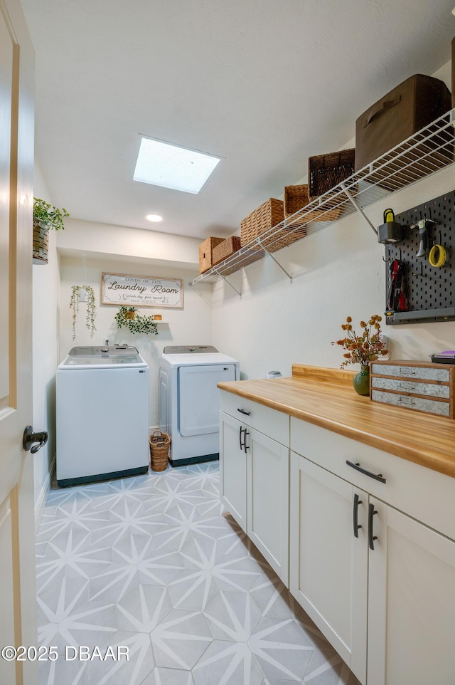 clothes washing area with cabinet space, light floors, a skylight, and washing machine and clothes dryer