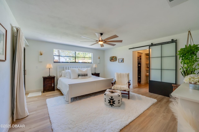 bedroom with visible vents, a walk in closet, a barn door, light wood finished floors, and ceiling fan