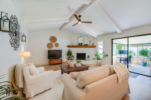 living area featuring lofted ceiling with beams, light wood finished floors, baseboards, a brick fireplace, and ceiling fan
