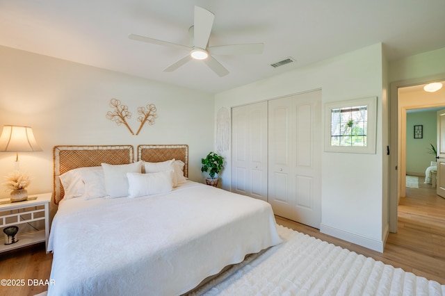 bedroom with visible vents, a ceiling fan, wood finished floors, a closet, and baseboards