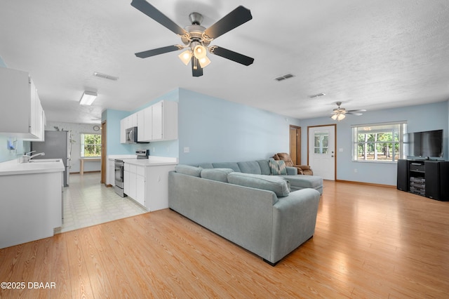 living room with ceiling fan, light hardwood / wood-style flooring, sink, and a textured ceiling