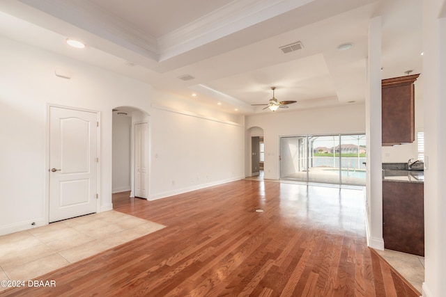 spare room featuring ceiling fan, a raised ceiling, light wood-type flooring, and crown molding