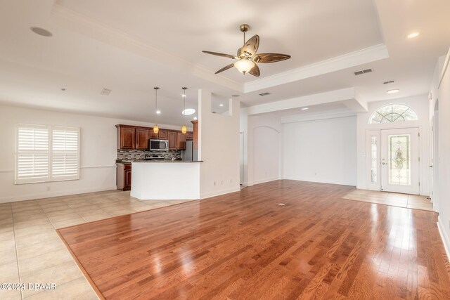 unfurnished living room featuring ceiling fan, light hardwood / wood-style floors, ornamental molding, and a tray ceiling