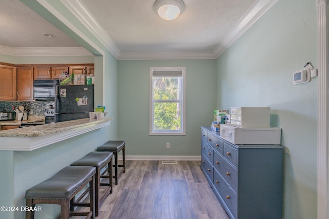 kitchen featuring hardwood / wood-style flooring, black appliances, light stone countertops, a breakfast bar area, and decorative backsplash