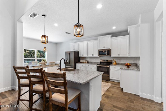 kitchen with stainless steel appliances, white cabinetry, dark hardwood / wood-style floors, light stone countertops, and hanging light fixtures