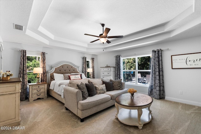 carpeted bedroom with multiple windows, a textured ceiling, ceiling fan, and a raised ceiling