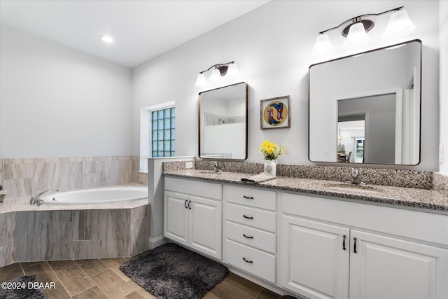 bathroom featuring hardwood / wood-style floors, vanity, and a relaxing tiled tub