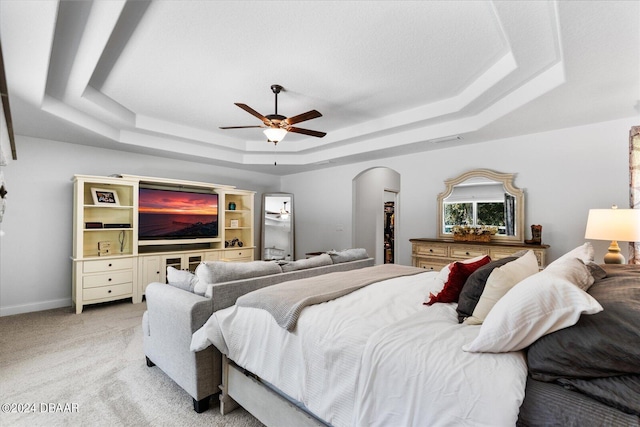 bedroom featuring a tray ceiling, light carpet, and ceiling fan