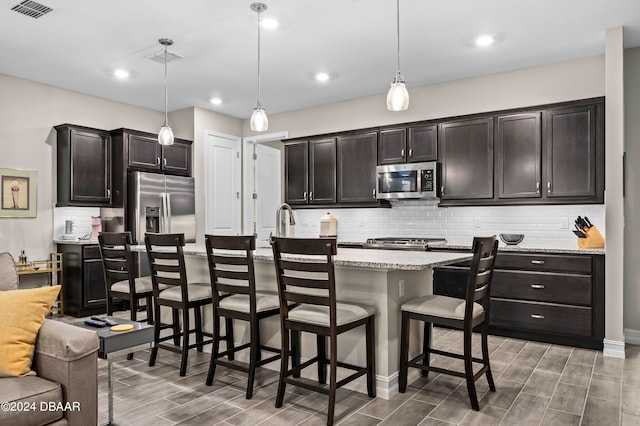 kitchen featuring a breakfast bar, dark brown cabinetry, stainless steel appliances, decorative light fixtures, and a center island with sink