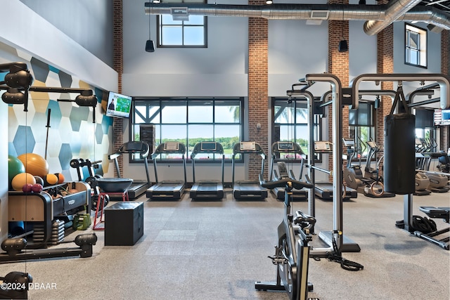 gym with a wealth of natural light, a towering ceiling, and brick wall