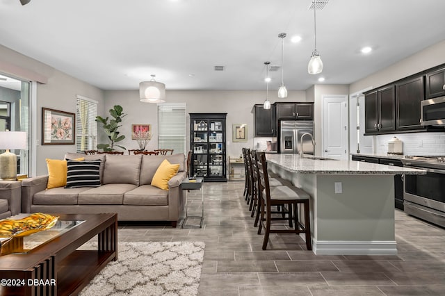 kitchen featuring a breakfast bar, stainless steel appliances, sink, a center island with sink, and hanging light fixtures