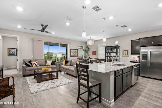 kitchen featuring ceiling fan, sink, light stone countertops, an island with sink, and appliances with stainless steel finishes