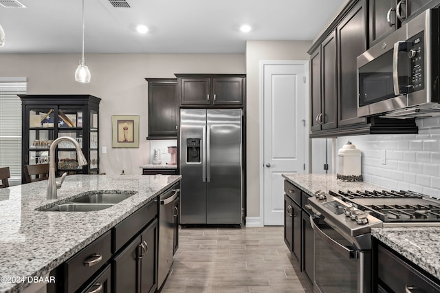 kitchen with light stone countertops, light wood-type flooring, stainless steel appliances, sink, and pendant lighting